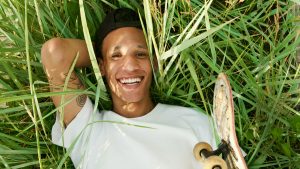 Young man lying in grass with skateboard